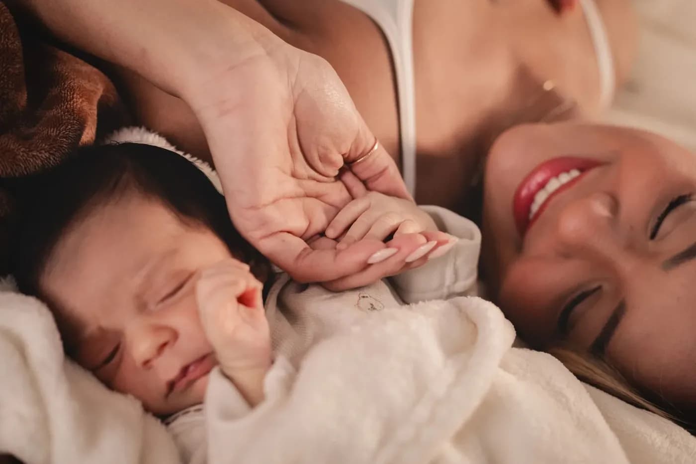 Una neomamma distesa accanto al suo neonato, che le tiene la mano.